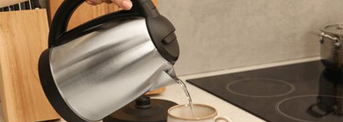 Woman pouring hot water from electric kettle into cup in kitchen,