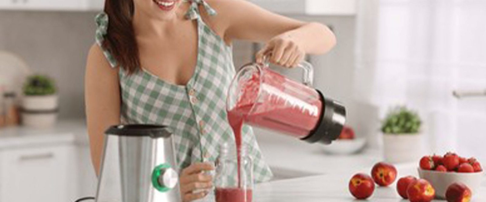 Young woman pouring fresh smoothie from blender cup into glass at